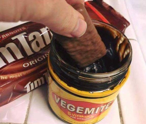 Someone dips a Tim-Tam Original into a jar of Vegemite. 