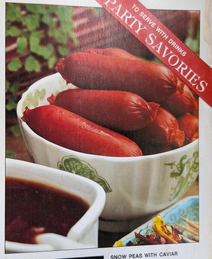 The recipe photo with an overlayed angled red strap on the top right saying "To serve with drinks/PARTY SAVORIES".

There is a ramekin with cocktail franks in the center of frame and presumably a gravy boat with the plum sauce running off the lower-left corner of the frame.