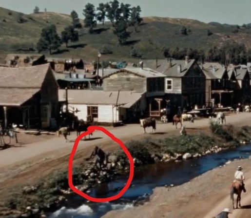 A still from Sora's "Historical footage of Californian gold rush" with an area circled in red where a cow/horse disappears and then a leathery black "something" appears and starts to grow.
