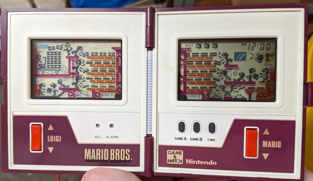 The inside of the game unit that splits horizontally into a left/right pair of screens and controls. Luigi is on the left and Mario on the right. The unit is in its initial power-on state showing every legend on its liquid crystal display.