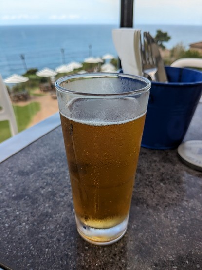 A half pint of beer with out of focus umbrellas and ocean in the background