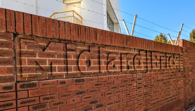 A red brick wall topped by barbed wire. The outline of "Midland Brick" has been chiselled out, leaving the text in the positive space.