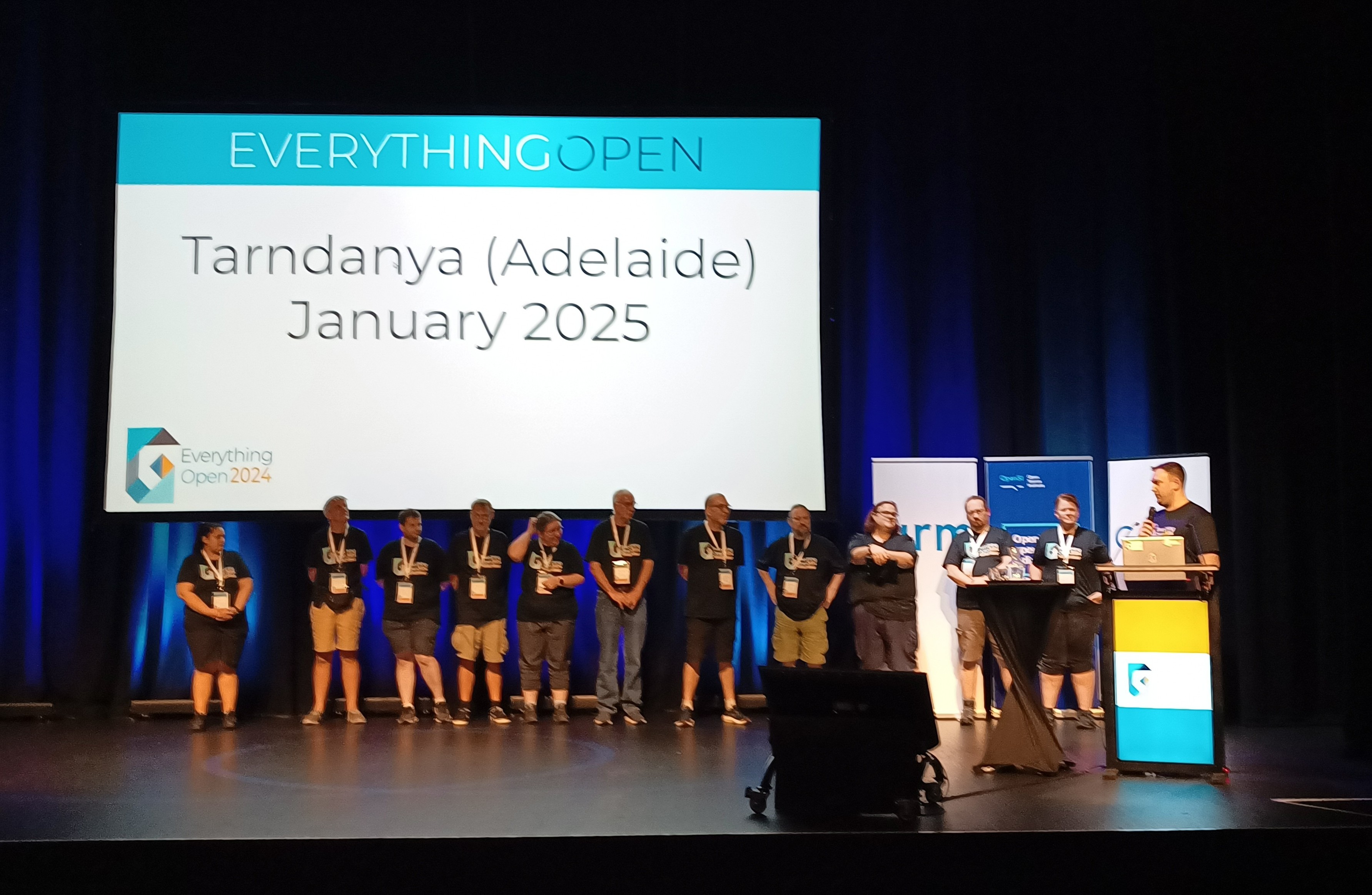 Organisers of the Everything Open conference on stage with screen announcing Tarndanya (Adelaide) in January 2025