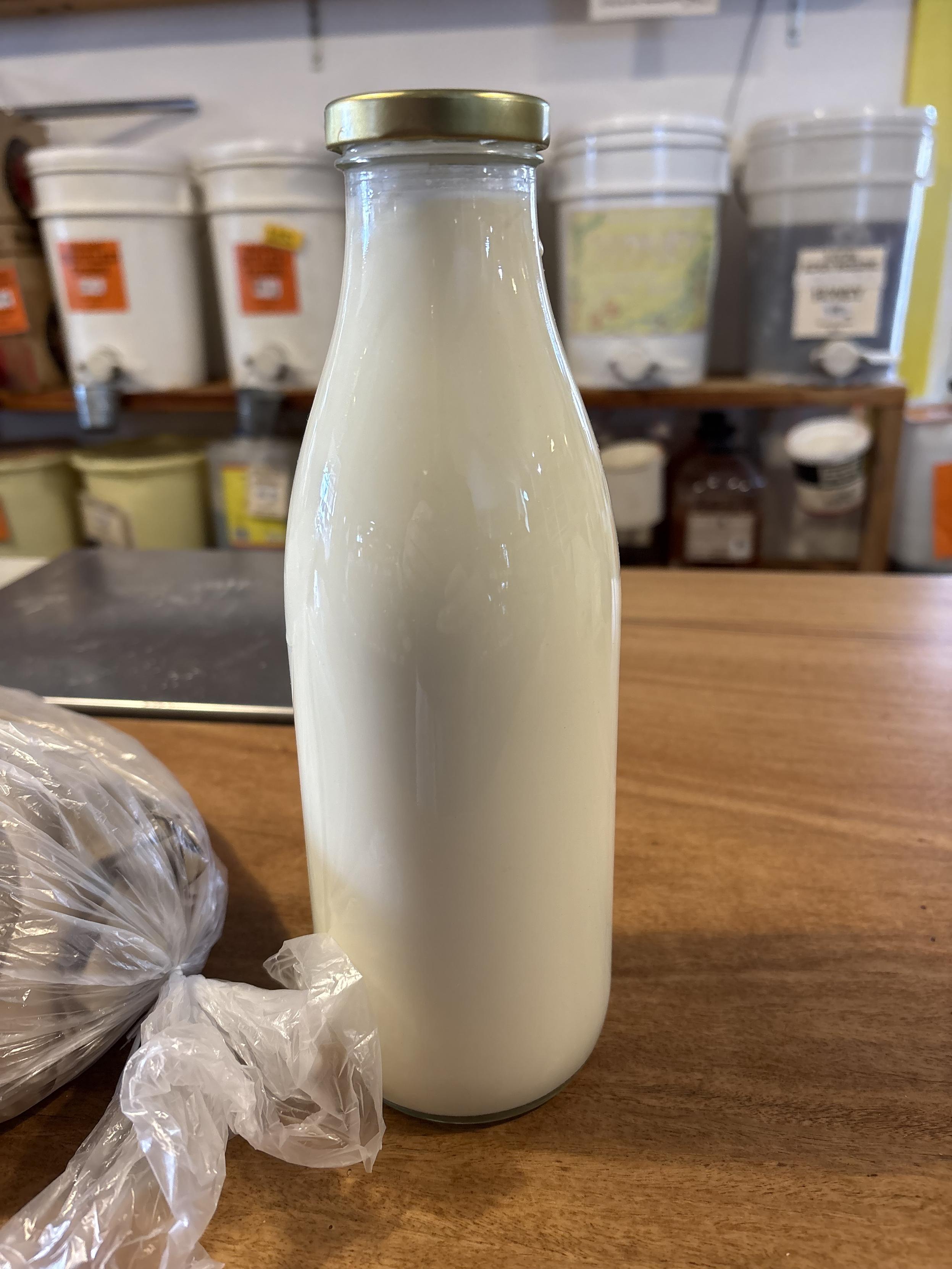 A refillable 1l glass bottle full of milk sits on a wooden counter top.