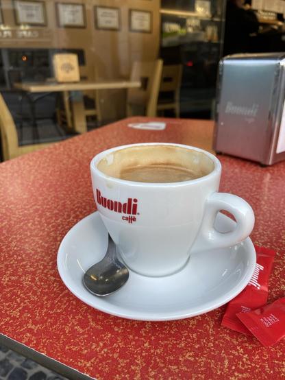 A partially drunk flat white (or its Portuguese equivalent) in a white cup on a red table 