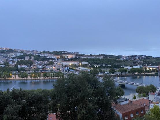 A view across a river at dusk with lights visible through windows of the buildings on a hillside