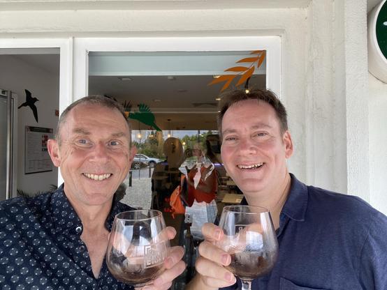 Two men hold beer glasses and smile at the camera 