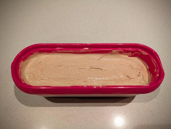 A long pink scoop tub of smoothed-over beige ice cream with little dark specks visible within it.
