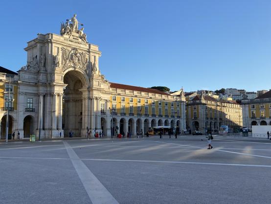 An arch and colonnade on a plaza under blue skies 