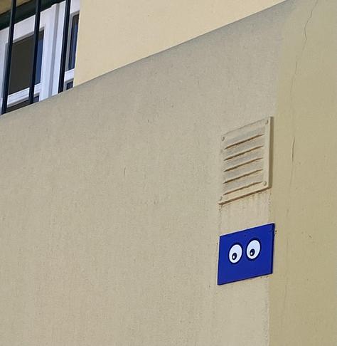 A pair of cartoon eyes affixed to a wall below a ventilation grate