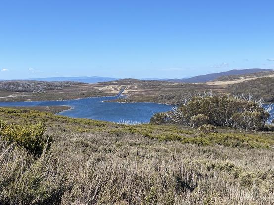 A blue reservoir surrounded by low shrub-covered hills under clear skies.
