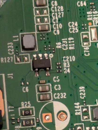 A close up photo of the power supply circuitry featuring many surface mount components. At the top left is a grey coil or transformer. Below it is a black 5-pin power regulator chip. Just at the left edge is the mounting for the input barrel jack and next to this are two tiny 0 ohm resistors.