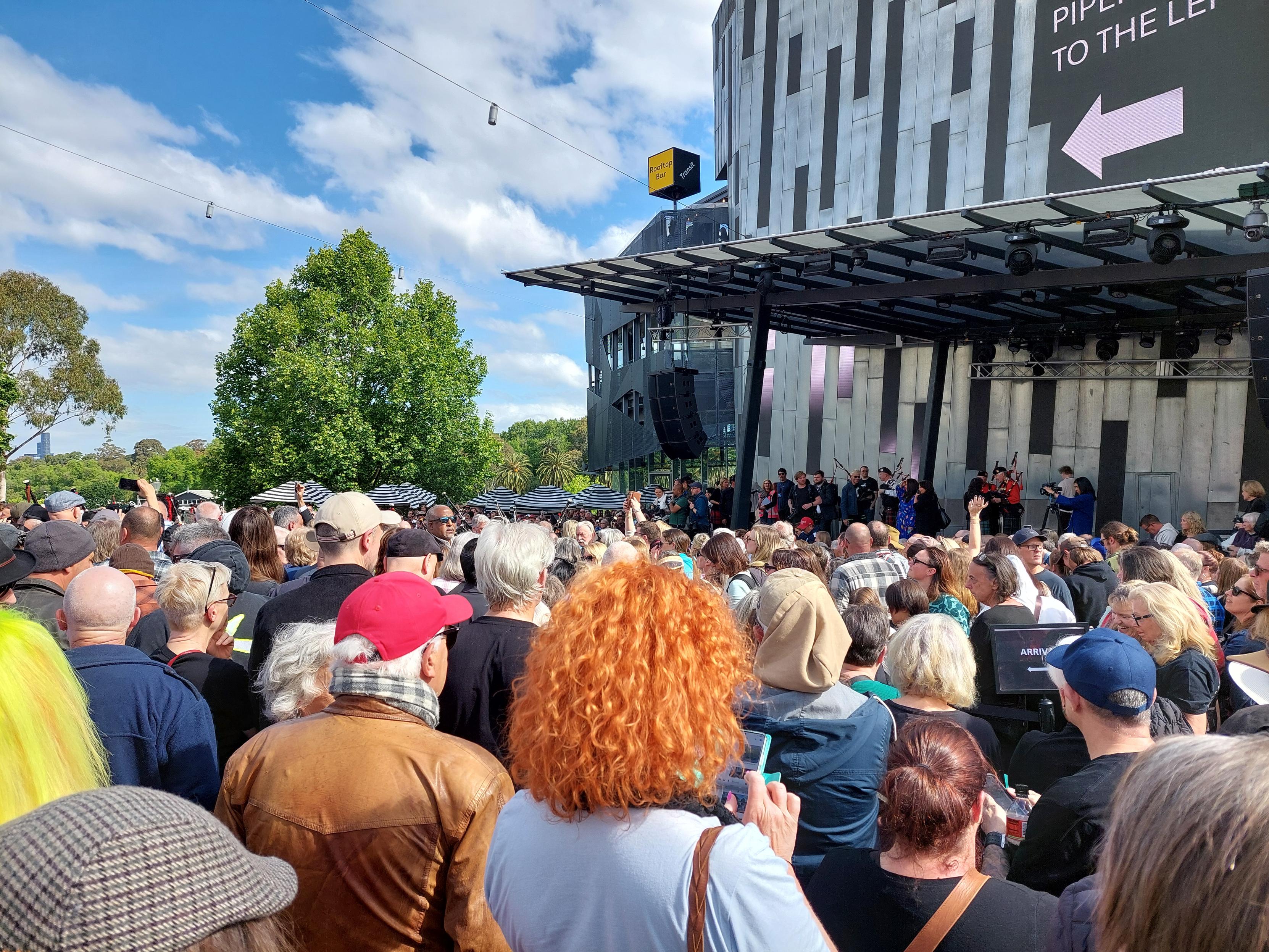 Backs of heads in a crowd. If you zoom in on the middle right you will be able to see some bagpipes. That is all that most of the crowd can see of the bagpipers!