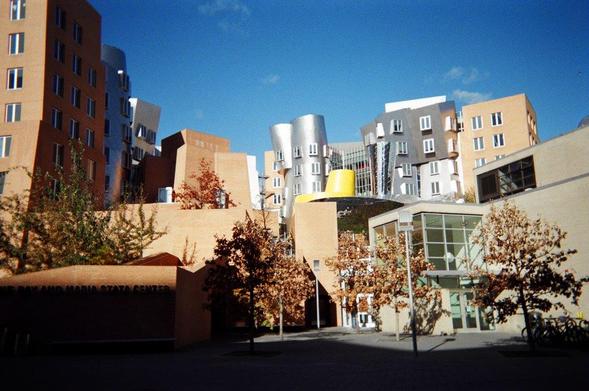 A modern building with towers clad in varying materials, some reflective, some brick, with trees in front and a blue skies above