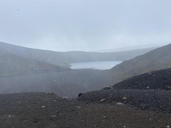 A volcanic lake under low clouds with light snow falling 