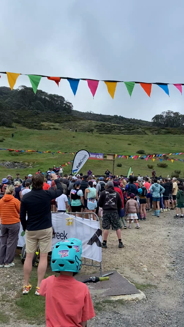 A large group of people set off on a trail run as the crowd counts down to zero. A mountain range is visible behind them under grey skies.