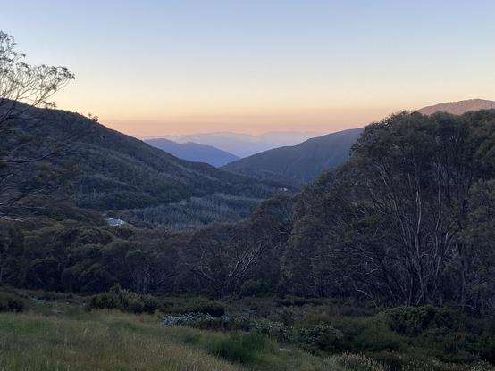 Darkening skies over a mountain valley with misty hills in the distance.