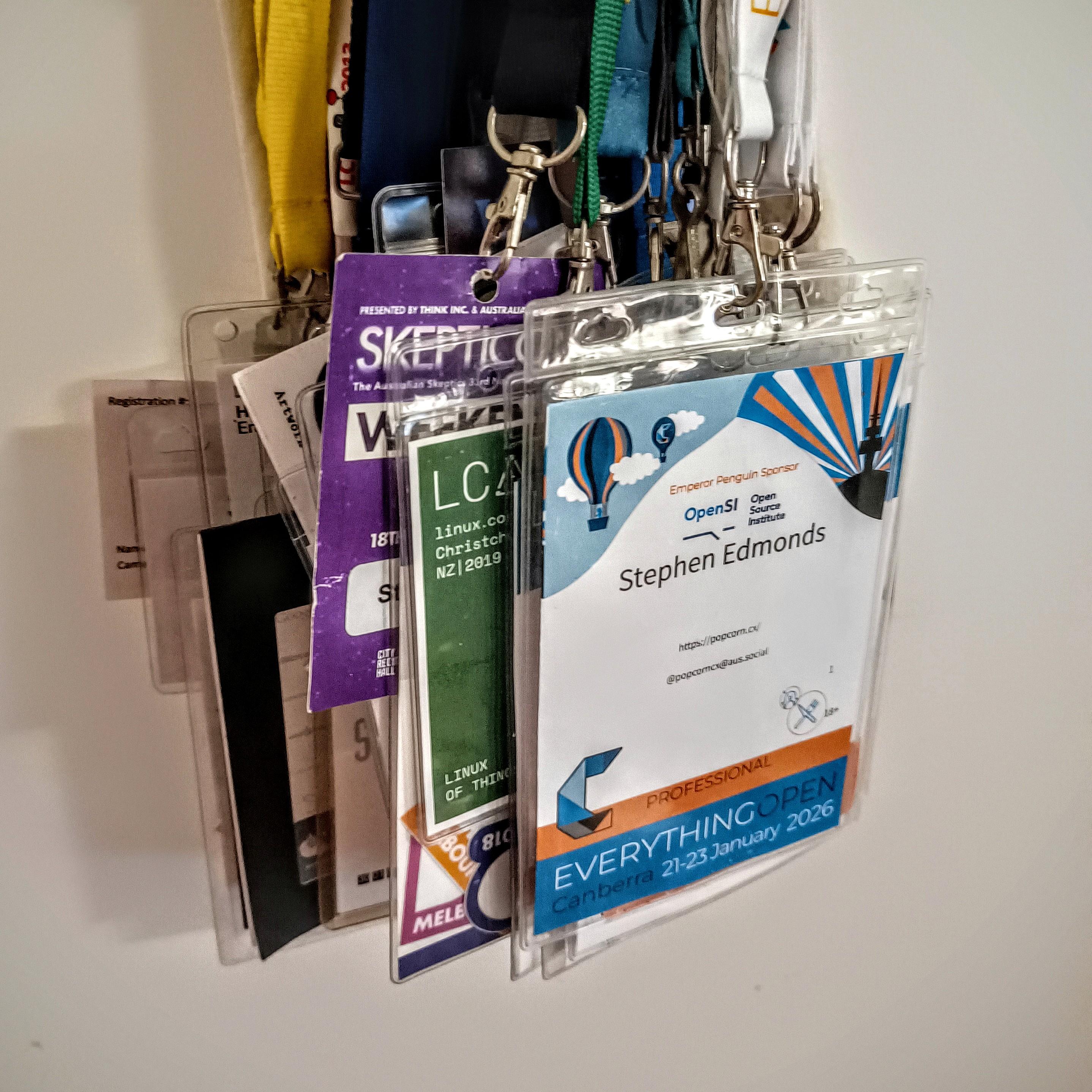 A collection of conference lanyards and nametags hanging behind a door, the frontmost one being for Everything Open 2026