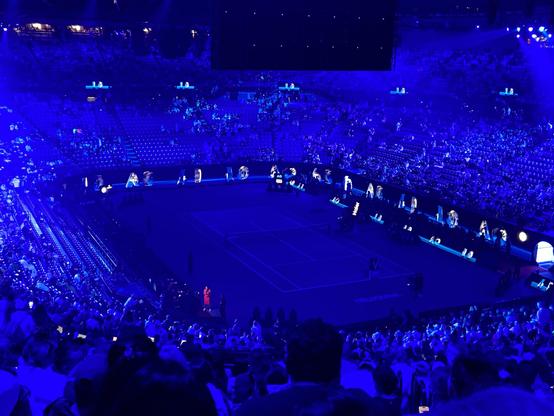 A tennis court bathed in dark blue light viewed from the highest row of seats 