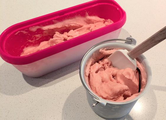 A pink scoop tub and an aluminium ice cream maker bucket with delicately pastel pink peach sorbet in them.