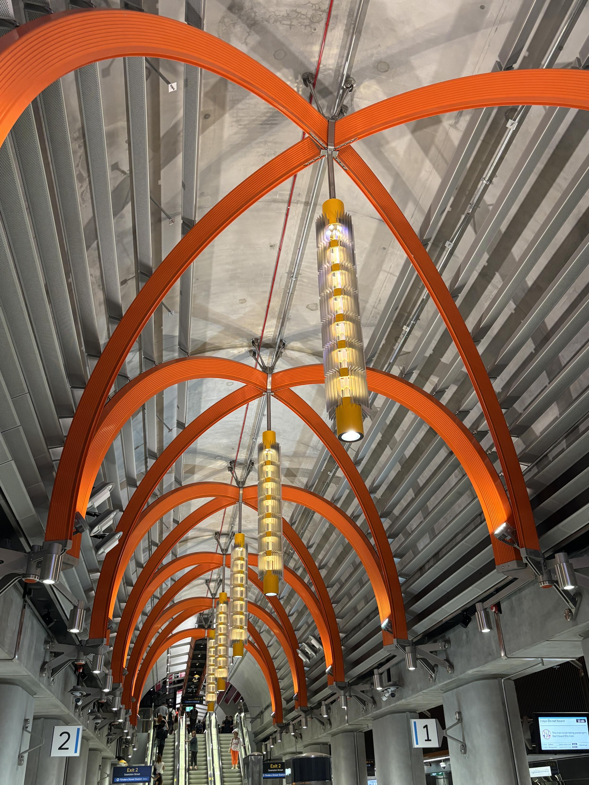 Vertical, cylindrical lamps hanging beneath orange beams.