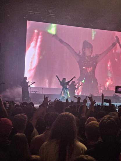 The lead singer of Babymetal on stage with her arms raised above her head. 