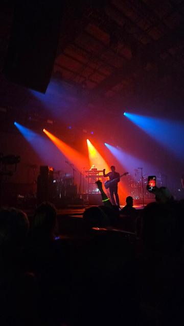 Moody dark tones with blue and red spot lights shining outwards. On stage a band is dimly lit. 