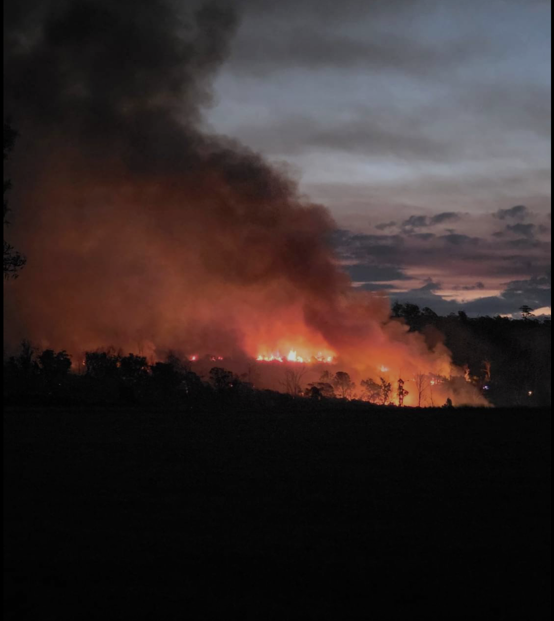 Sunset with a bushfire below. It glows dark orange with a huge plume of smoke.
