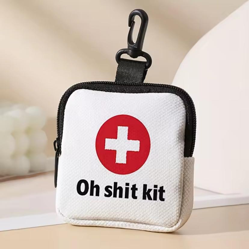 A first aid kit bag with carabiner, about 150mm square bearing the swiss cross and the text “Oh shit kit”