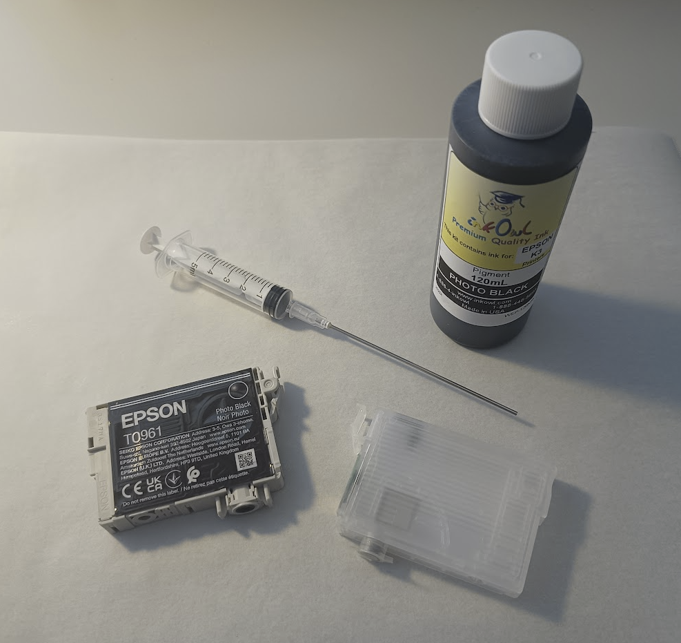 An Epson ink cartridge alongside an empty refillable cartridge, a syringe and a bottle of ink.