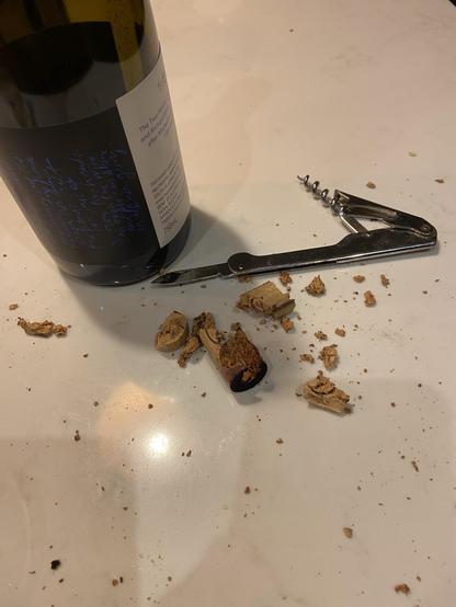 A wine bottle, a classic corkscrew, and a lot of cork crumbs on a countertop