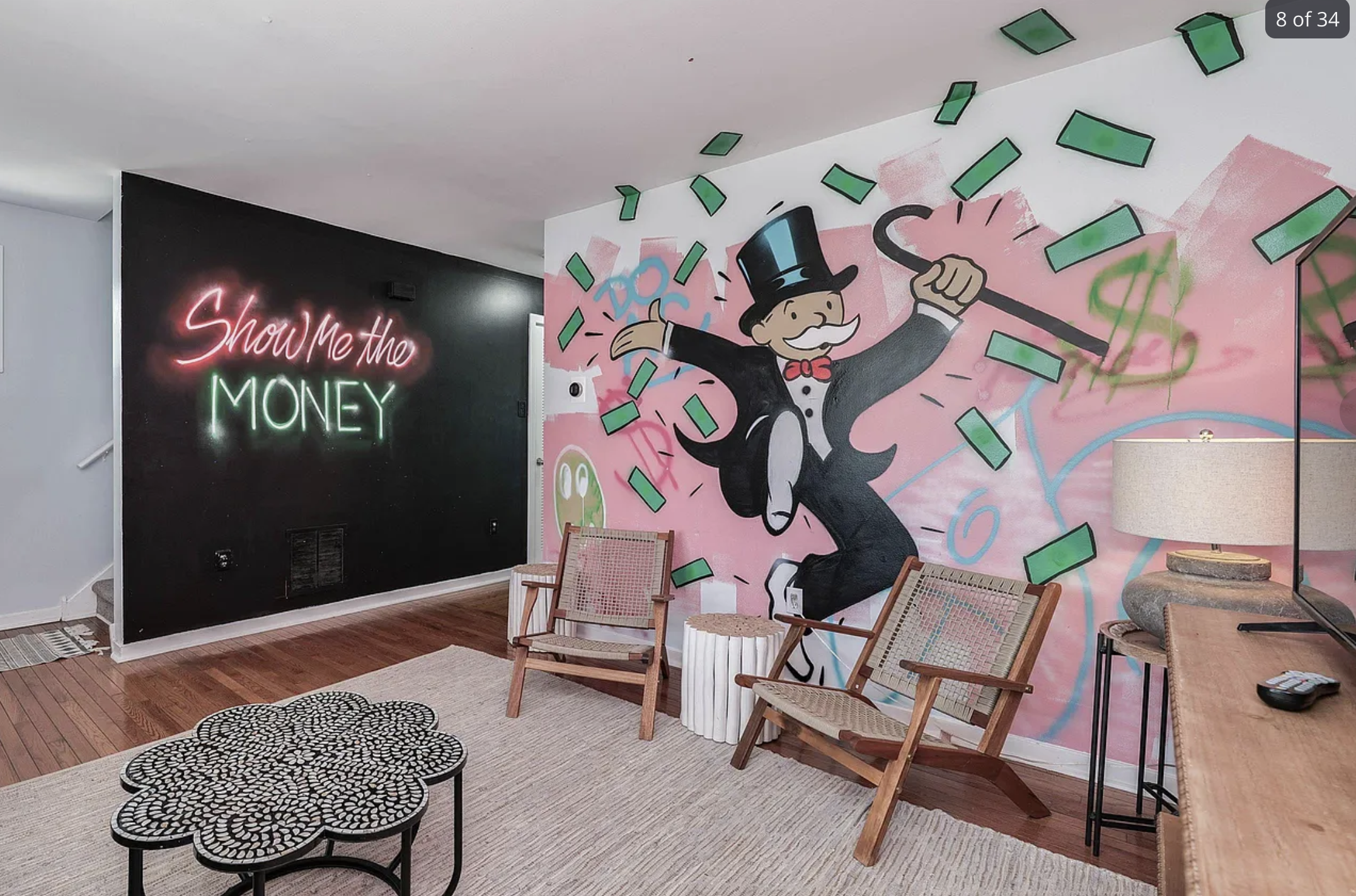 A living room with a wall mural of the Monopoly guy with money flying all around, and another wall that says show me the money in neon letters