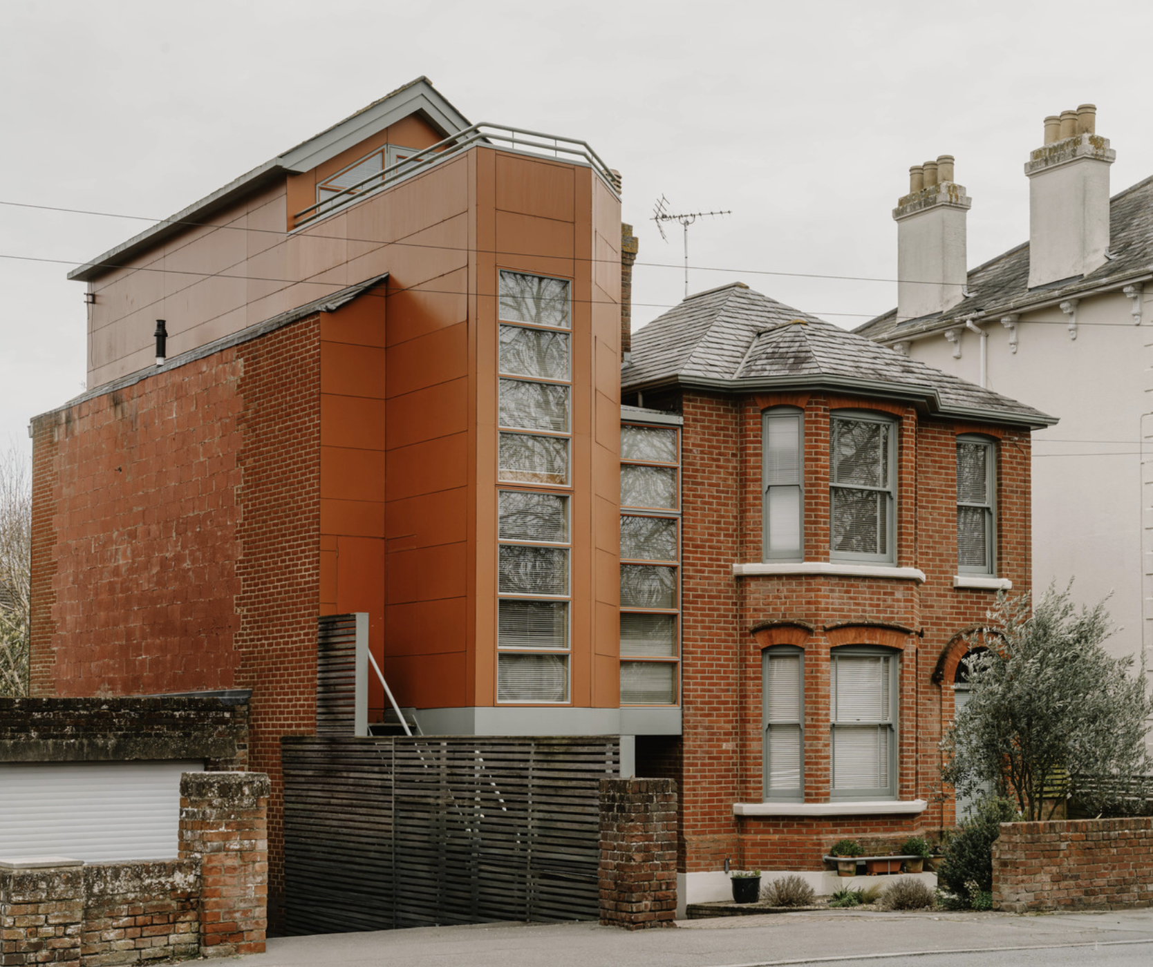 A house in 2 connected parts - the one on the right is brick and old fashioned with 2 stories and bay windows, and the left is a completely modern structure that looks like an office building with 2 columns of rectangle glazing that are at least 3 stories high.