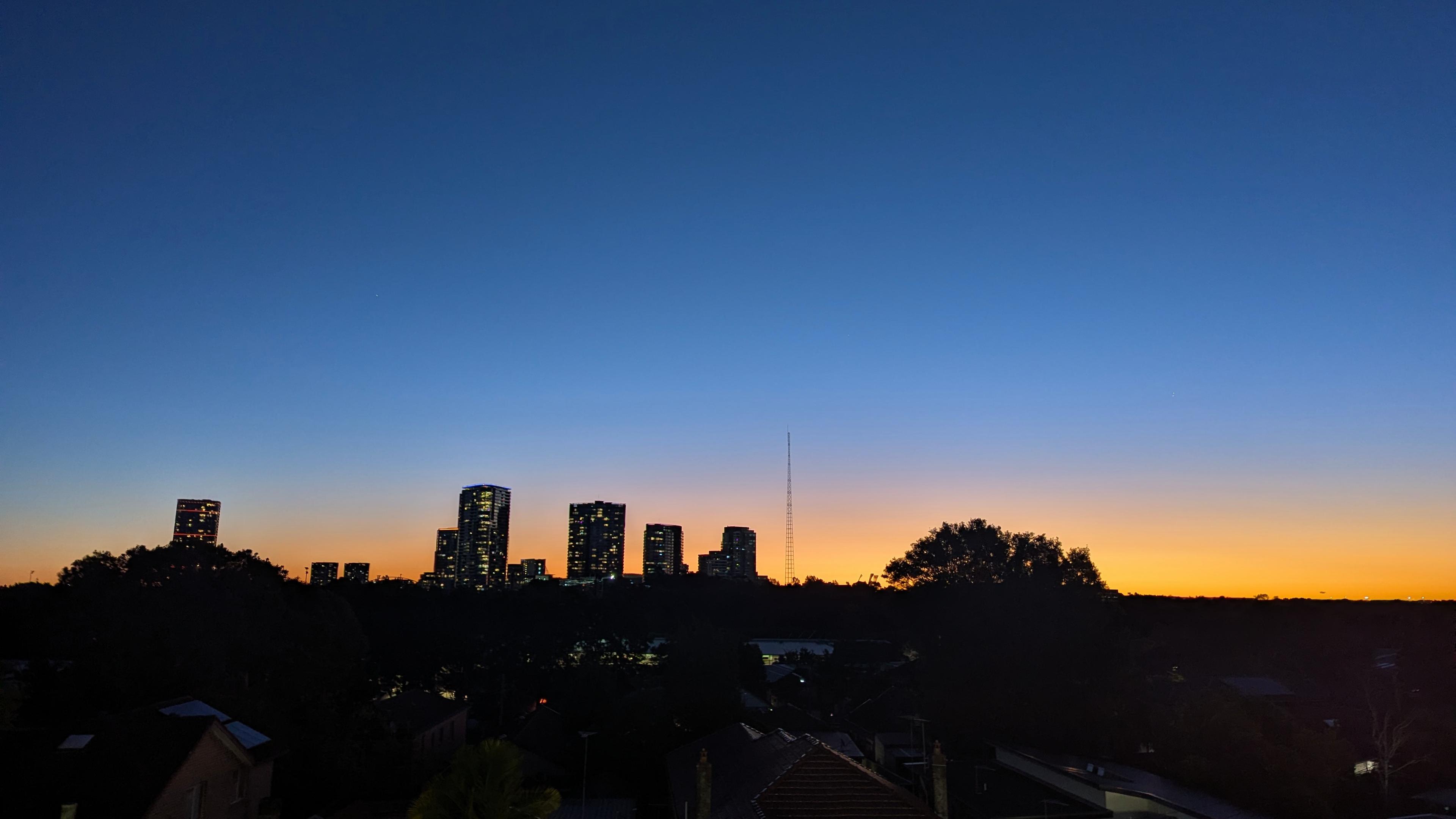 Photo of a skyline at dusk, with towers silhouetted against an orange horizon.