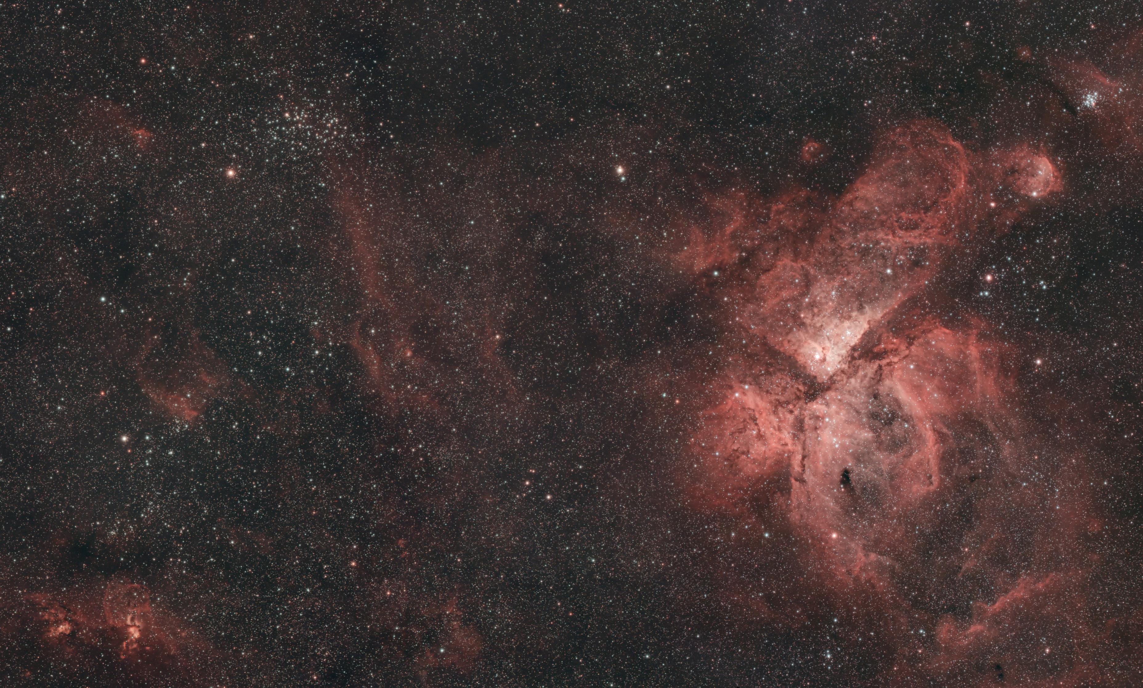 Image of a large area of sky, dominated by a big bright nebula on the right, with several smaller ones plus a few star clusters, and many, many stars scattered everywhere.