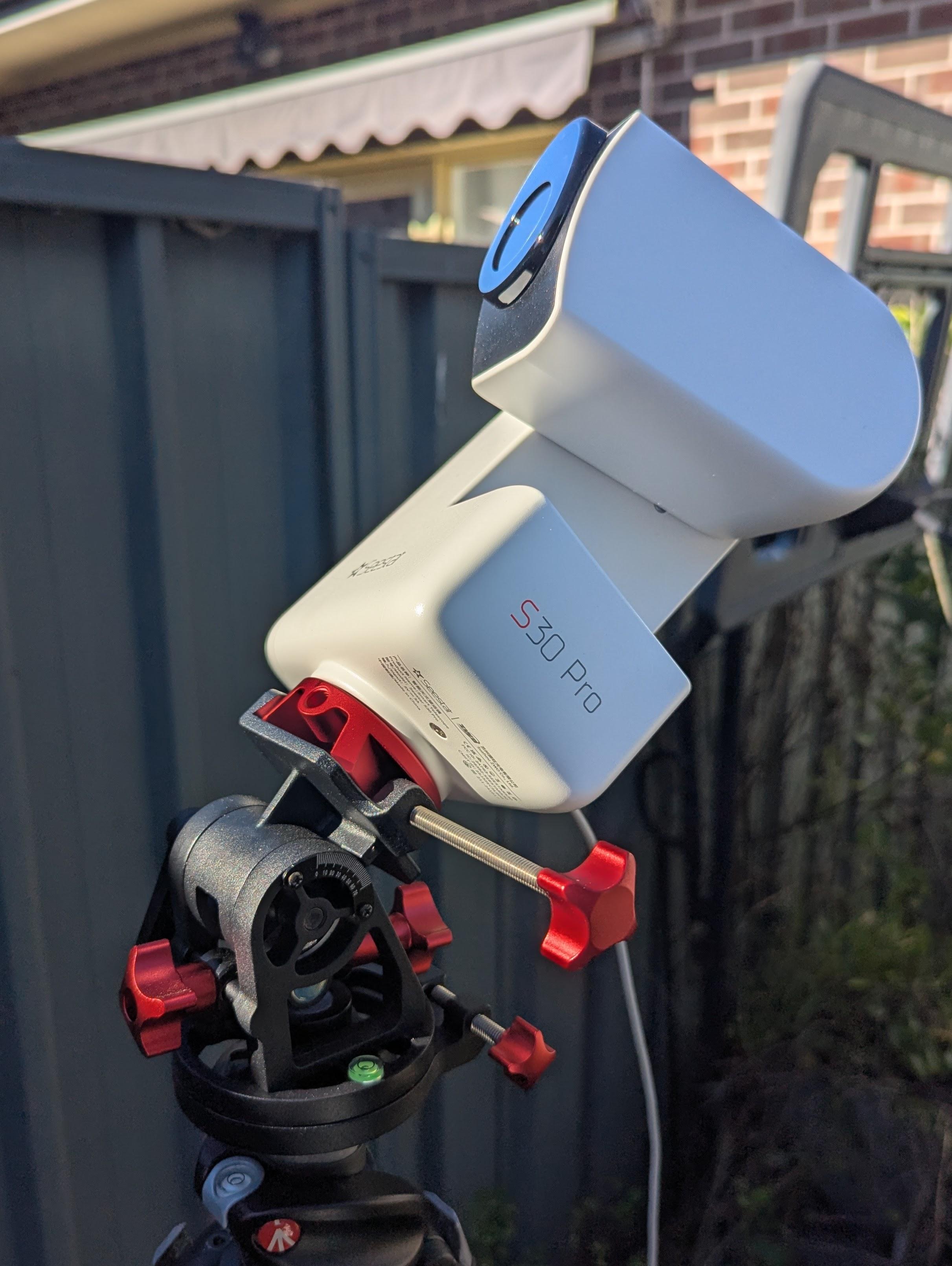 Photo of a Seestar S30 Pro smart telescope on a tripod during the day. There is a solar filter attached to the telescope, which is pointing towards the Sun.