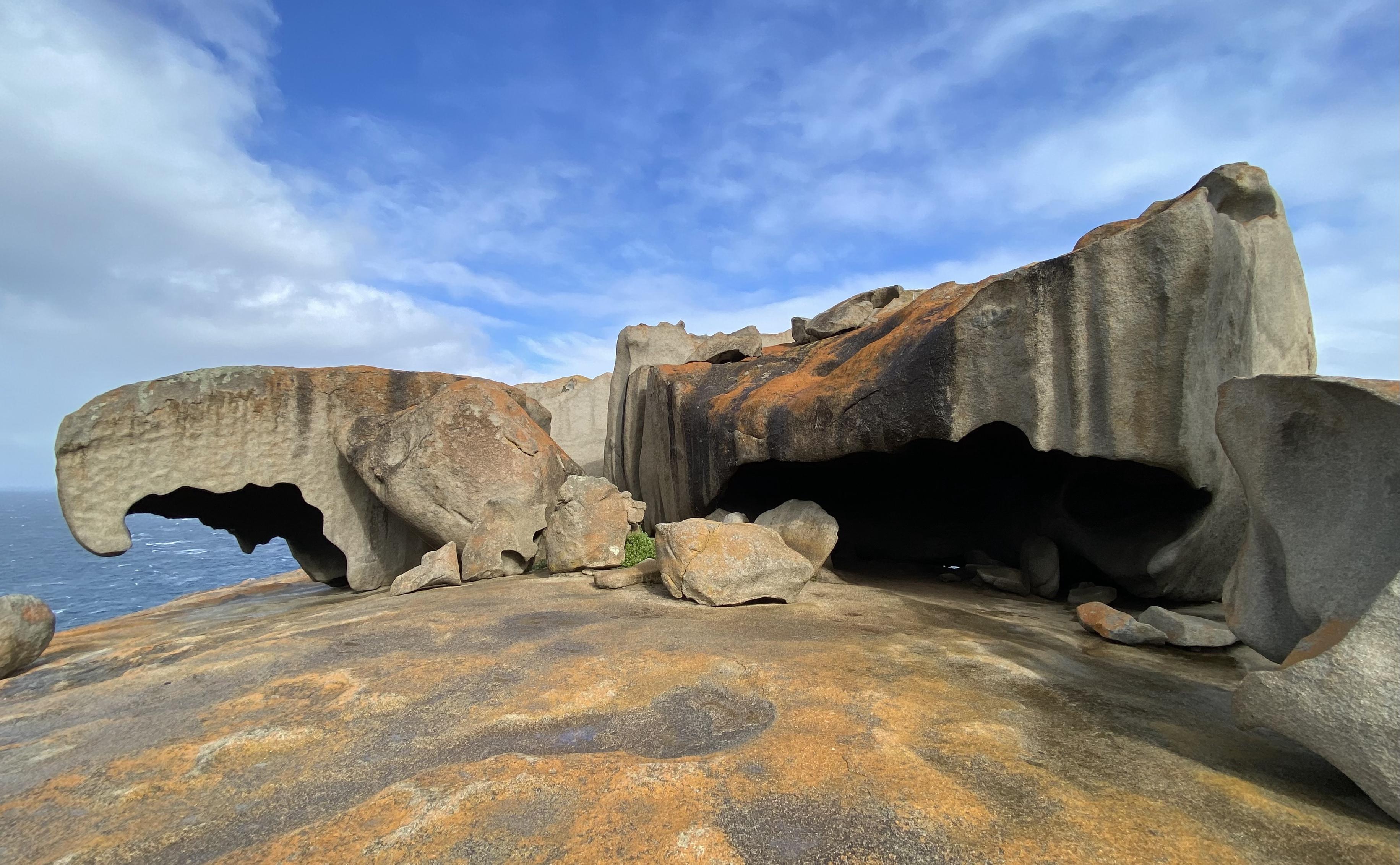 Granite rocks, eroded and coloured by lichen, against a grey choppy sea and blue sky with lots of cloud.