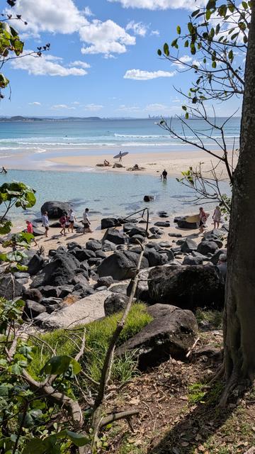People walk on the sand, a baby plays in the water, kids make sand castles and surfers reorganise for their next run around the calm pool behind the sand bar at the Eastern end of Coolangatta Beach.