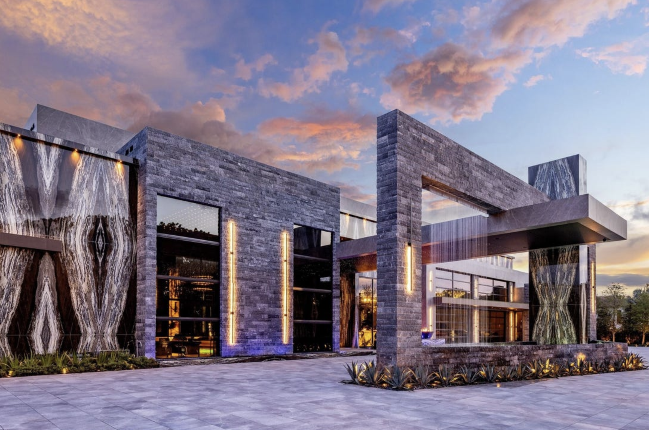 The outside of a house with large marble panels looking like the Eye of Sauron, there is also a sculptural waterfall out front. It's very modern and a bit confusing.