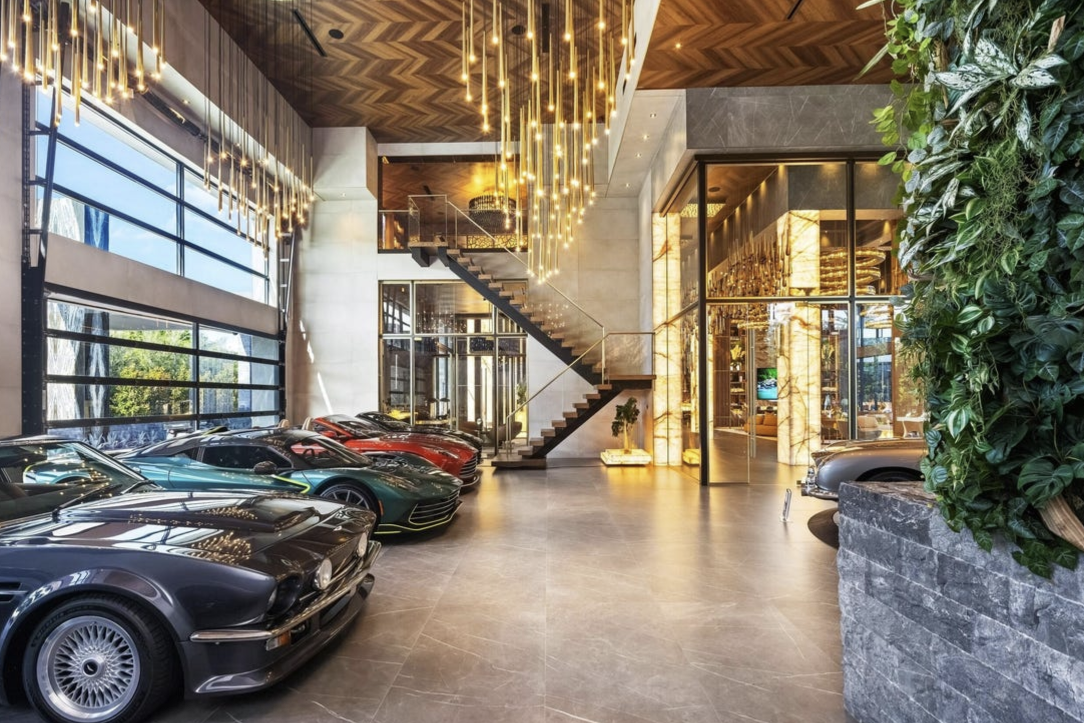 A garage full of expensive cars that is open to the rest of the house, there are yet more chandeliers, an open staircase and some plants