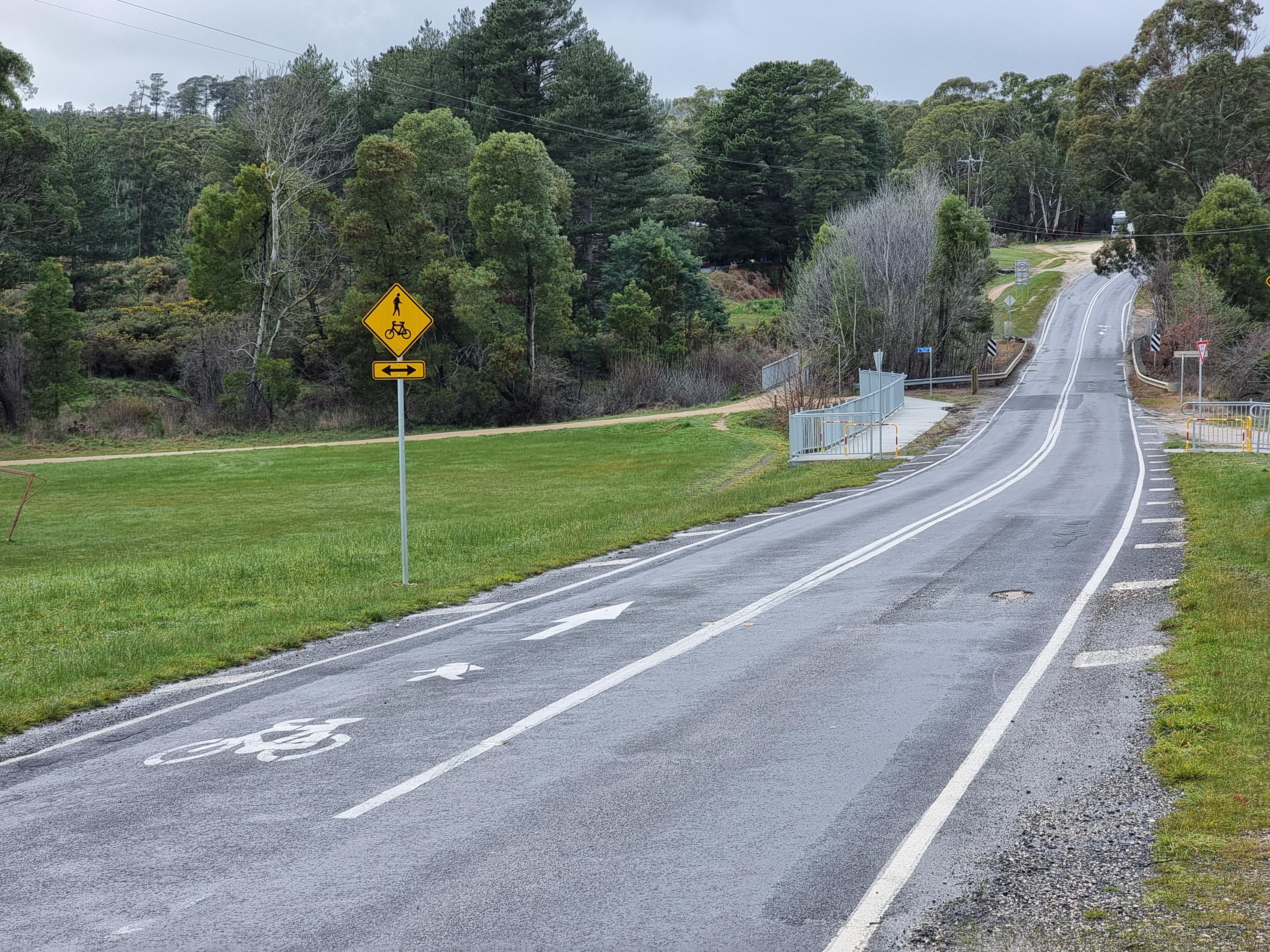 A forward arrow, pedestrian symbol, and bicycle symbol, marked in the left lane of a two lane road. An 80 km per hour sign can be seen in the distance.