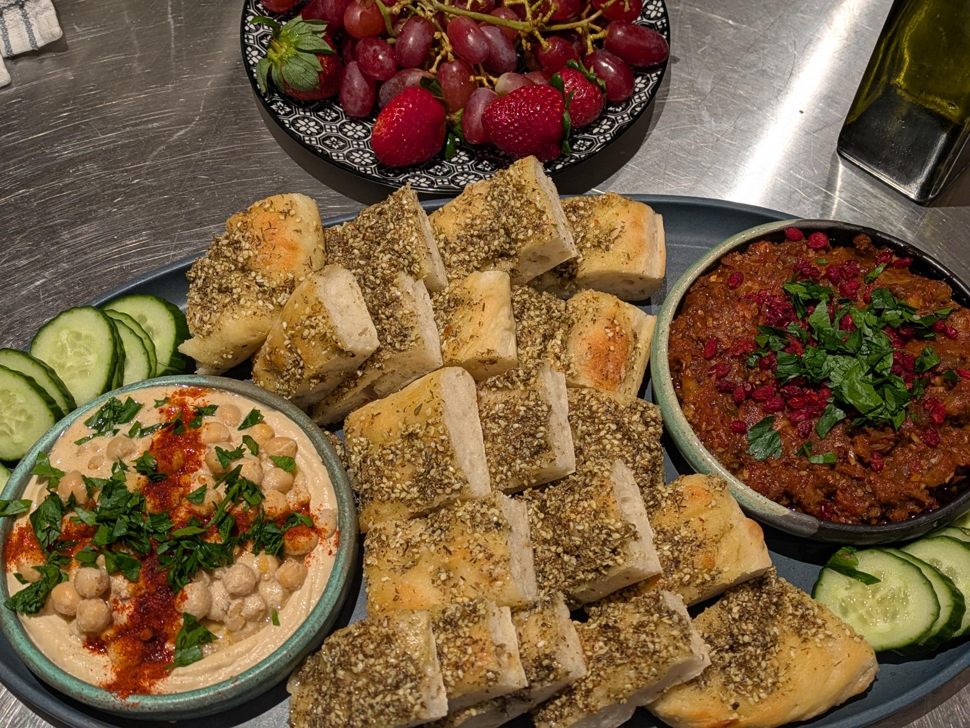 Home made hommus topped with chickpeas, home made zaatar flat bread, and an eggplant tomato dip, arranged on a platter.