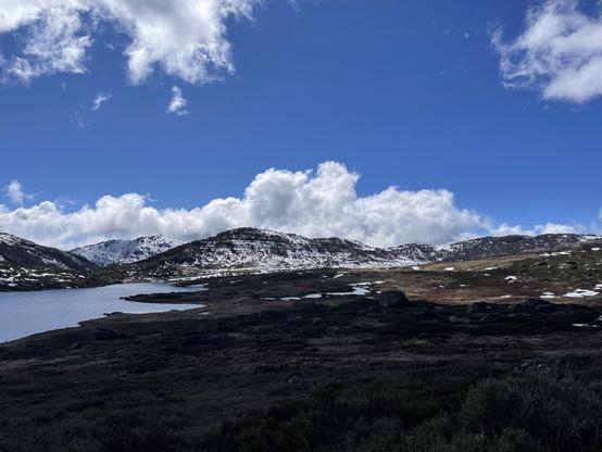 Snow covered mountains above a lake under blue skies with light clouds