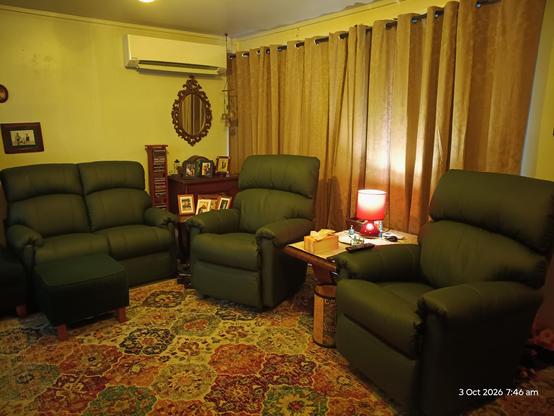 A green leather two seater sofa and 2 recliners placed on a bright rug in a mellow old fashioned room.